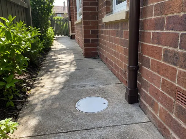 Brick side path with a circular drain cover set in concrete beside a downpipe in Cammeray