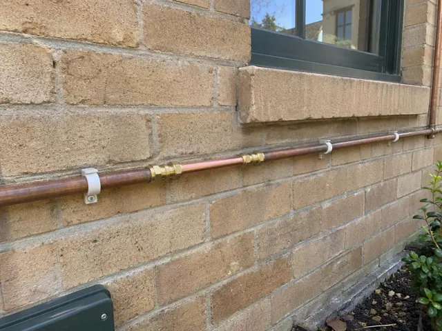 Repaired copper water pipe fixed to a brick exterior wall below a window in North Sydney