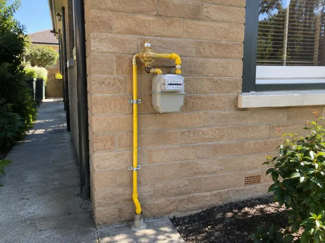 Yellow gas meter and repaired pipework on a brick exterior wall beside a window in Wollstonecraft